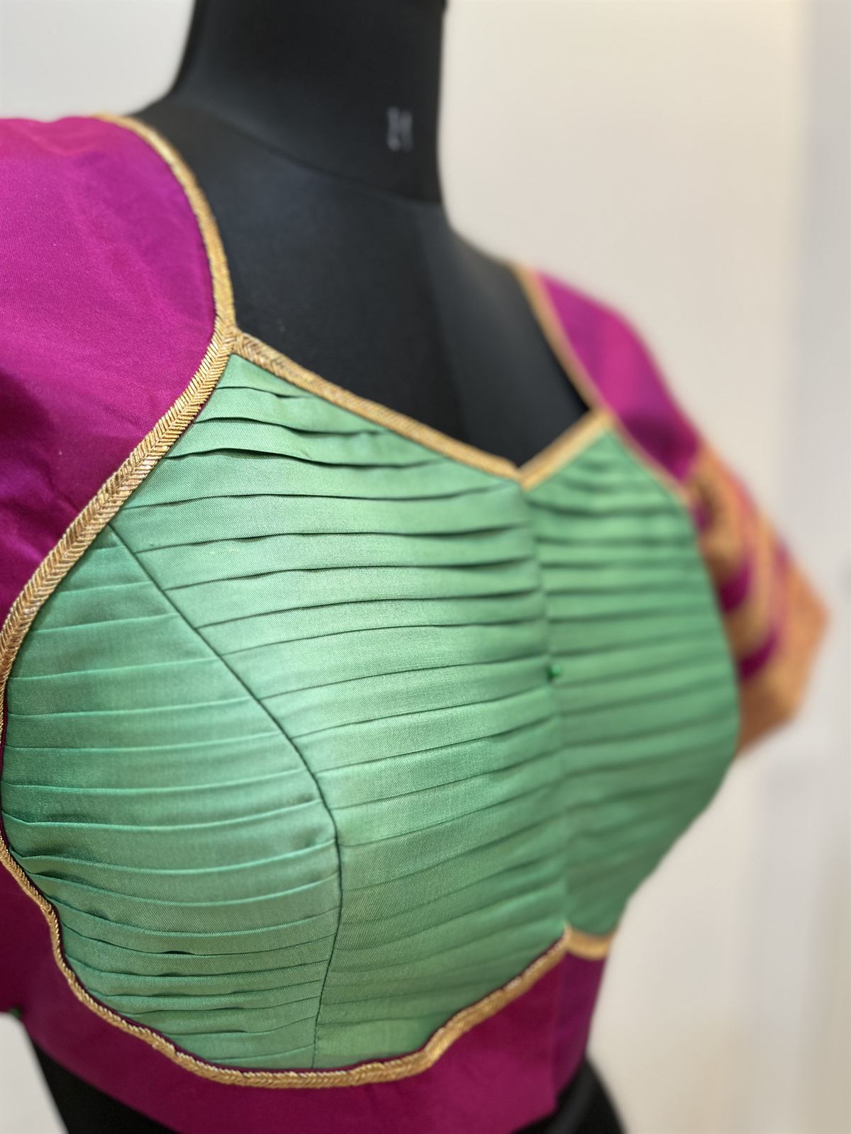 Magenta blouse with a sage green pintucked front panel and gold piping, fitted on a dress form